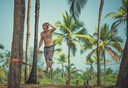 India, Goa - January 9, 2017: The guy walks on a rope against the background of palm trees.のeditorial素材