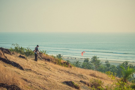 India, Goa - November 28, 2016: A man mows the grass against the background of the beach and the sea.のeditorial素材