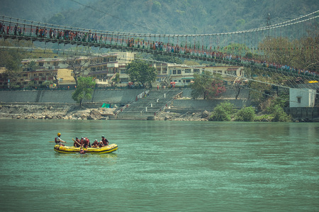 Rishikesh. India. April 12, 2017: People in a yellow boat sailing along the Ganges River under the bridger.のeditorial素材
