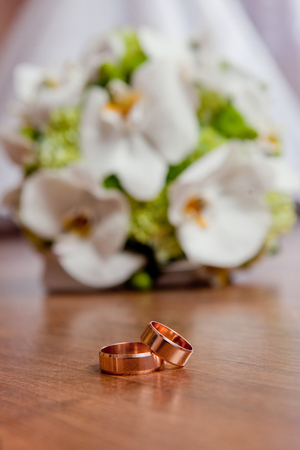 Beautiful wedding rings lie on a table against the background of a bouquet of flowers.の写真素材