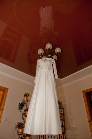 Beautiful wedding dress hanging on the lamp in the room with a shiver in the ceiling. Wedding Morning.の写真素材