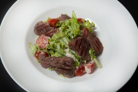 Veal salad, salad with large slices of veal and fresh vegetables on a plate on a black backgroundの写真素材