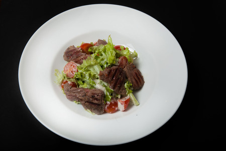 Veal salad, salad with large slices of veal and fresh vegetables on a plate on a black backgroundの写真素材