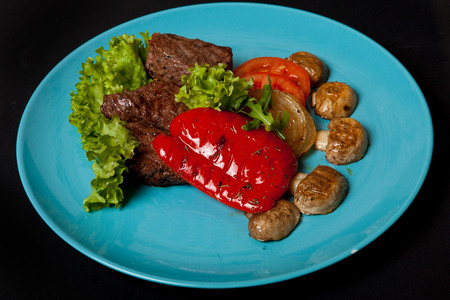 Medallions of veal with grilled vegetables on a black background, top view.の写真素材