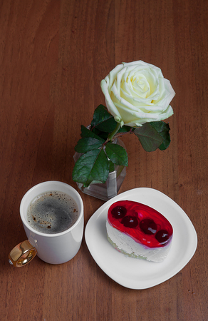 A cup of coffee with a cake and a rose on a wooden background. Valentine's Day.の写真素材