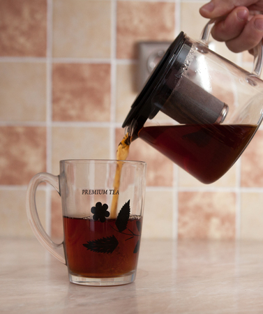 A glass kettle and a glass cup with tea on the table. From a transparent kettle pours pouring tea into a mugの写真素材