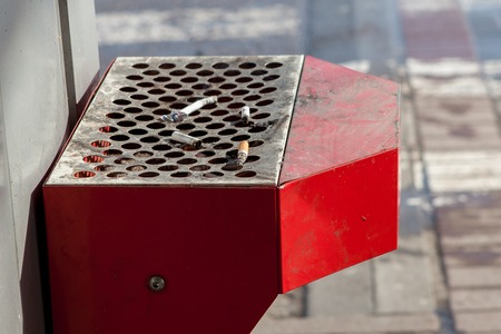Street trash can with ashtray and cigarette butts. Trash can tied to the fence.の写真素材