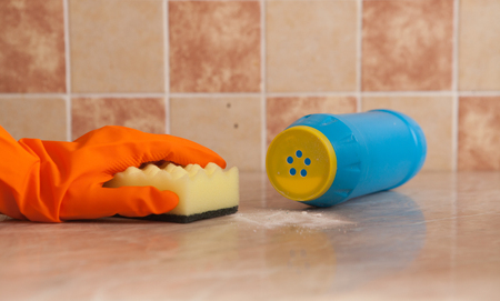 Hand in orenge rubber gloves wash the surface of the with a soft yellow sponge near the scratched detergent.の写真素材