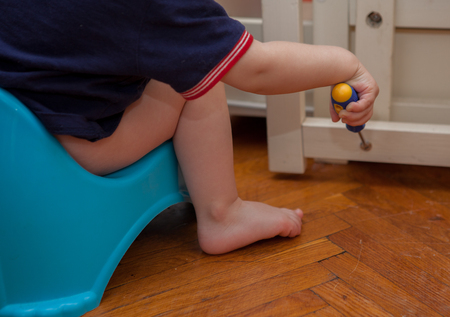 The child sits on the pot and repairs his bed.の写真素材