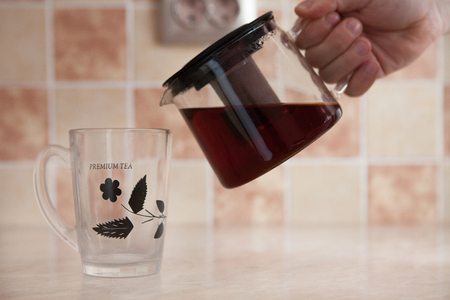 A glass kettle and a glass cup with tea on the table. From a transparent kettle pours pouring tea into a mugの写真素材