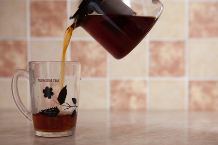 A glass kettle and a glass cup with tea on the table. From a transparent kettle pours pouring tea into a mugの写真素材