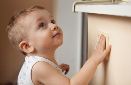 A small child, boy or girl, looking up and reaching to a light switch.の写真素材
