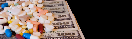 Pills on dollar money isolated on black background. Medicine expenses. High costs of medication concept. Place for textの写真素材