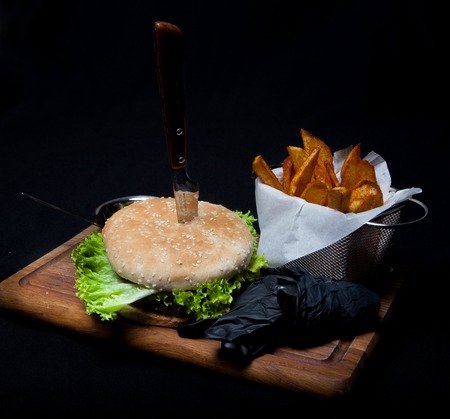 Tasty grilled beef burger with lettuce, cheese and onion served on cutting board with french fries on a black wooden table.の写真素材