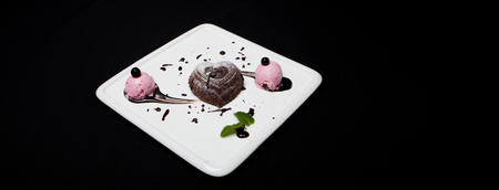 Dessert fondan chocolate with ice-cream on a white plate on a black background. Exquisite French chocolate dessert fondan, place for text.の写真素材