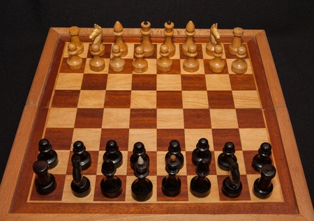 Black and white wooden chess pieces on board with black background.の写真素材