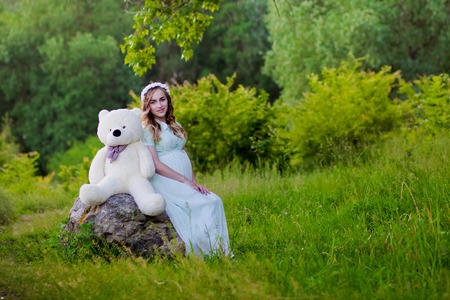 Beauty pregnant woman relaxing in the park and holding a teddy bear.の写真素材