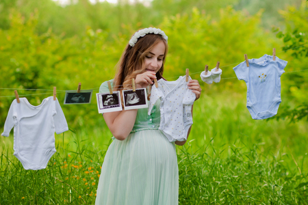Beautiful pregnant woman outdoor hanging childrens clothes. Great time.の写真素材