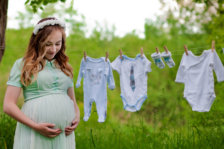 Beautiful pregnant woman outdoor hanging childrens clothes. Great time.の写真素材