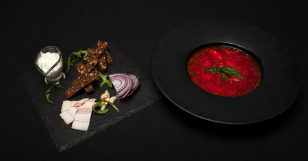 Salted lard with pepper and black bread lies on a plate, next to it there plate with red borsch.. Close-up, top view.の写真素材