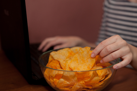 Young happy woman eating chips near a computer. Unhealthy concept.の写真素材