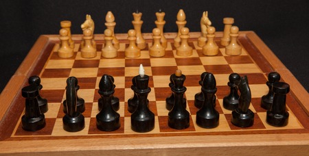 Black and white wooden chess pieces on board with black background.の写真素材