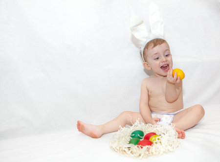Portrait of baby boy with bunny ears headband, playing with easter eggs, isolated on white...