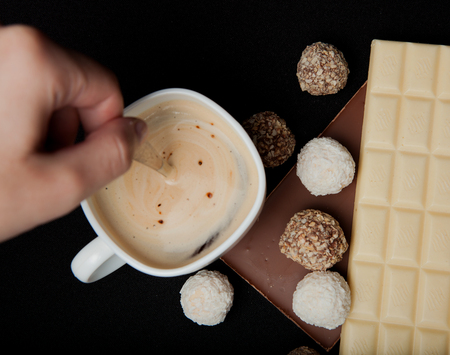 Woman adding sugar in coffee in cafe. Cofe, Stack of Black and White Chocolate isolated on black background, place for text.の写真素材