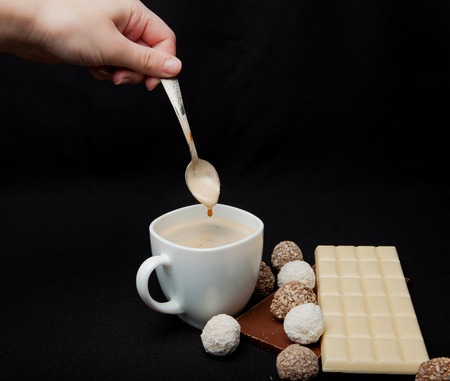 Woman adding sugar in coffee in cafe. Cofe, Stack of Black and White Chocolate isolated on black background, place for text.の写真素材