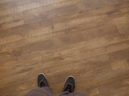 top view to man's legs as horizontal lines. Close up view on man's legs in brown pants and brown sneakers against wooden floor. Toned picture.の写真素材