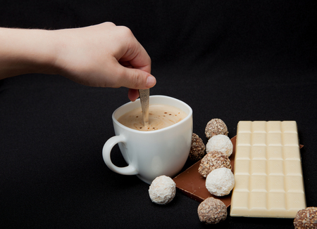 Woman adding sugar in coffee in cafe. Cofe, Stack of Black and White Chocolate isolated on black background, place for text.の写真素材