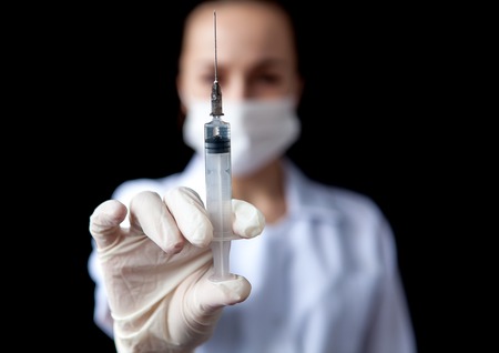 Blurred image of nurse holding syringe in hand on black background.の写真素材