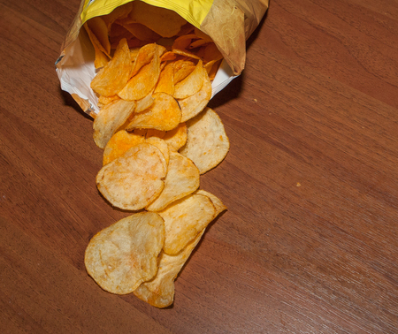 Potato chips on a wooden background, top view. Salty crisps scattered on a table.の写真素材