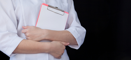 Front view of a young intellectual healthcare doctor in labcoat on black backround. Doctor with a notebook in his hands with free space for text.の写真素材