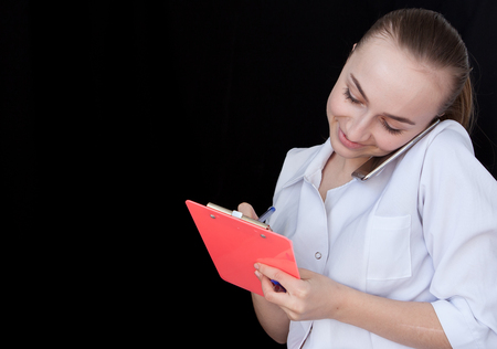 Front view of a young intellectual healthcare doctor in labcoat on black backround. Doctor with a notebook in his hands with free space for text.の写真素材