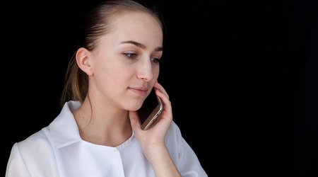 Front view of a young intellectual doctor on a black background with text space. The medical worker talking on a cell phone.の写真素材