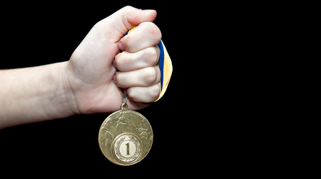 Woman hand holding gold medal against black background. Award and victory concept.の写真素材