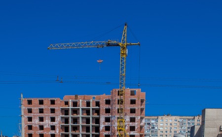Construction site of a new apartment high building with tower cranes against blue sky. Residential area development. Real estate project growth concept.の写真素材