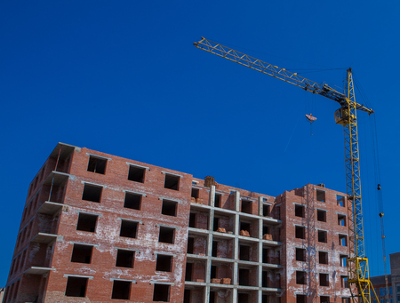 Construction site of a new apartment high building with tower cranes against blue sky. Residential area development. Real estate project growth concept.の写真素材