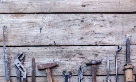 Old, rusty tools lying on a black wooden table. Hammer, chisel, hacksaw, metal wrench. Copy spaceの写真素材