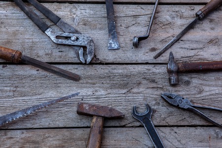 Old, rusty tools lying on a black wooden table. Hammer, chisel, hacksaw, metal wrench. Copy spaceの写真素材