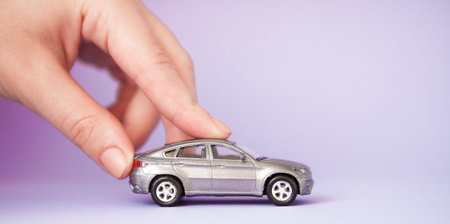 Toy child car in woman's hand. Purchase insurance bank loan travel where to go trip journey concept. Isolated on violet.の写真素材