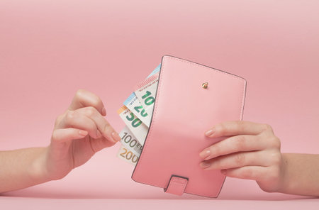 Pink purse and Euro banknotes in Female hands on pink background