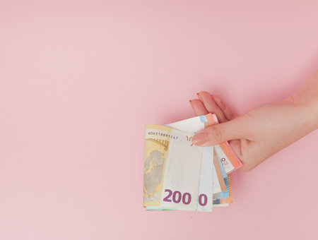 Euro banknotes money in female hands on pink background.