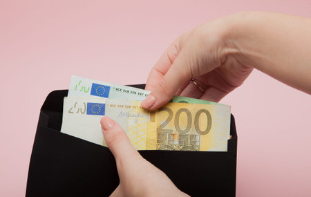 Women hands put euro in black envelope on pink background.