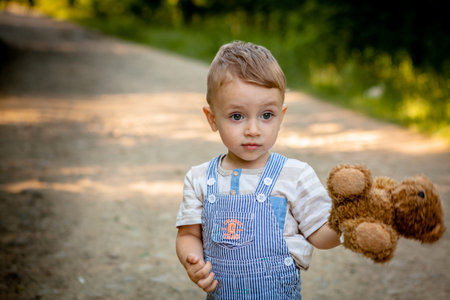 Little boy playing with teddy bear on the footpath.
