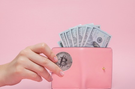 Pink wallet with Dollars and bitcoin in woman's hand on a pink background with copy space.の写真素材