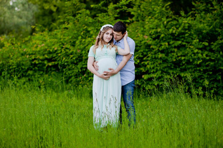 A man look the tummy of his beautiful pregnant wife in the park.