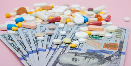 Dollars and pills on a pink background. Prescription medicine on dollars for pharmaceutical industry concept of high cost for healthcare and medication, top view.の写真素材