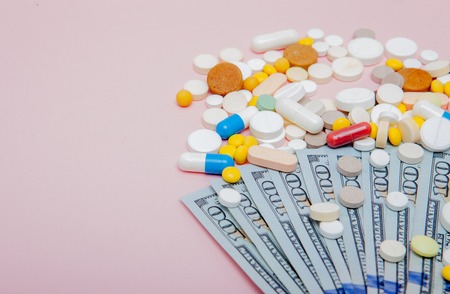 Dollars and pills on a pink background. Prescription medicine on dollars for pharmaceutical industry concept of high cost for healthcare and medication, top view.の写真素材